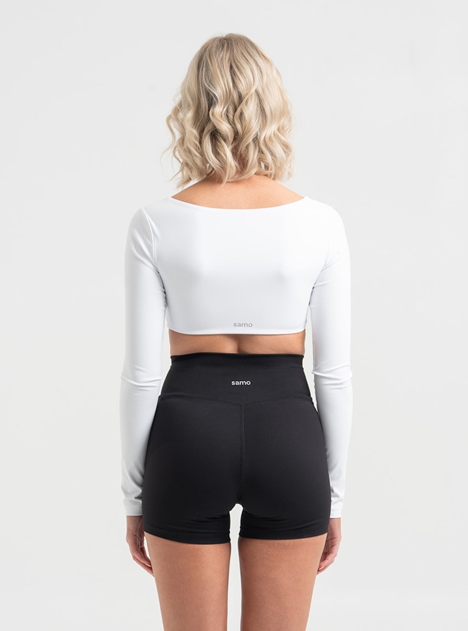 Frau trägt weißes Cropped Longsleeve und schwarze Cross Over Shorts von shop-samo.com